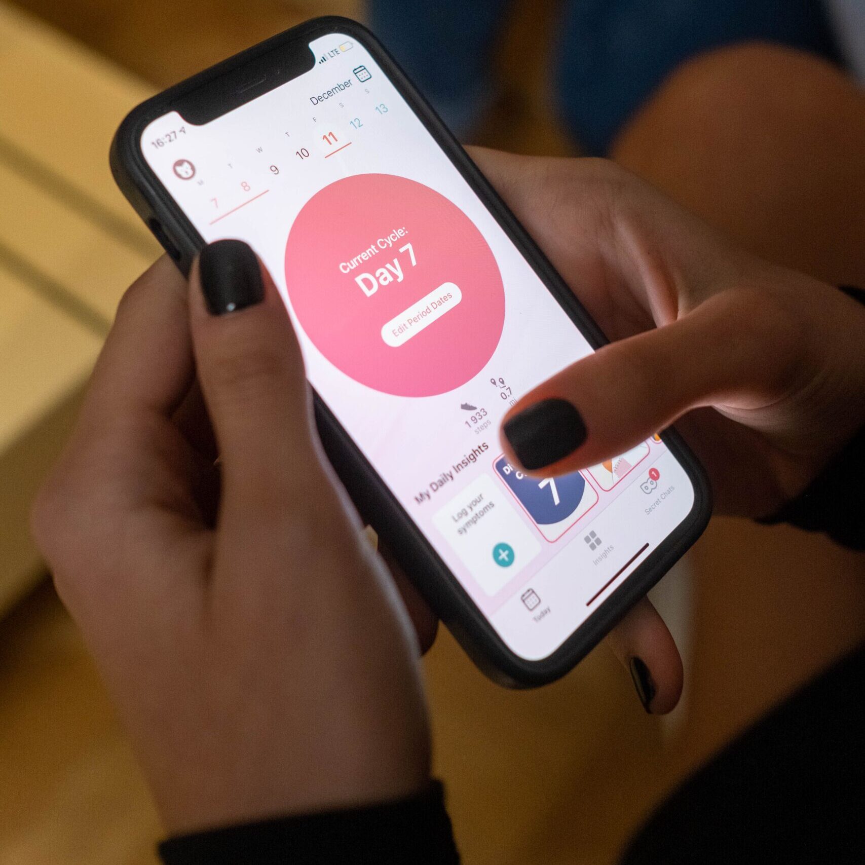 Close-up of a woman using a menstrual tracking app on her smartphone indoors.